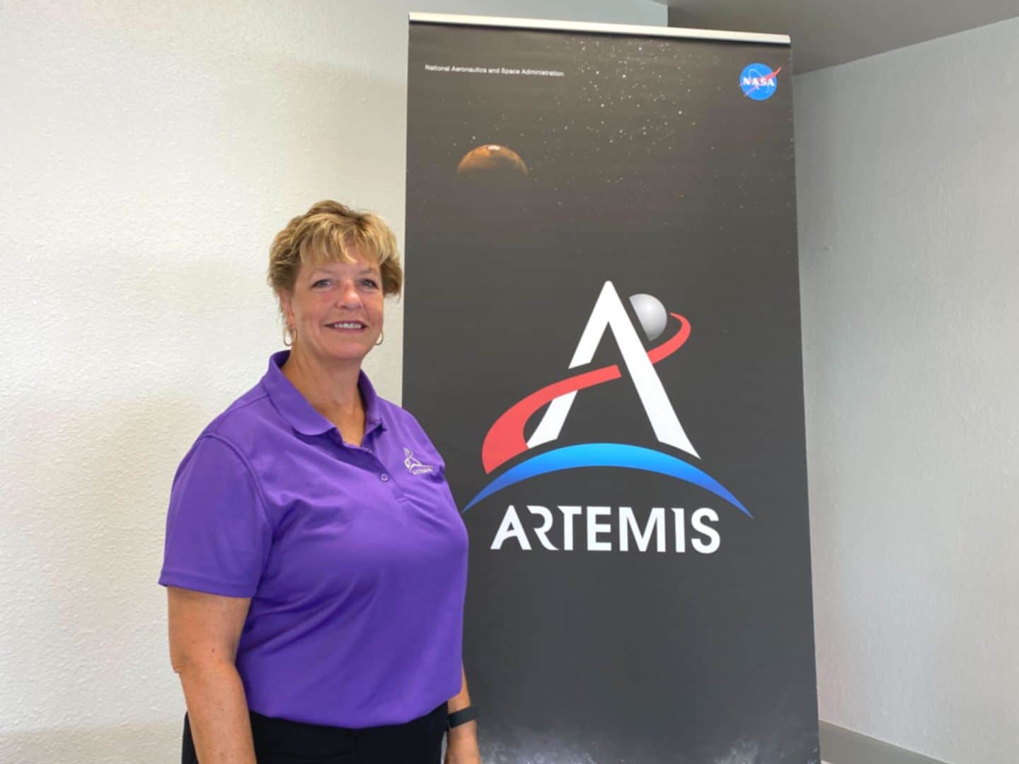 Annette Hasbrook, NASA Orion Senior Advisor stands in front of an Artemis Program banner
