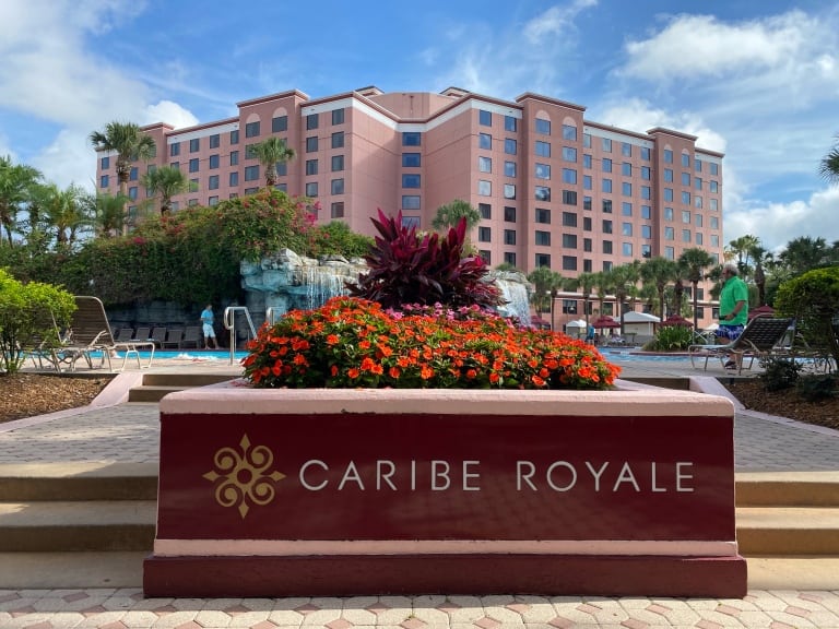 Caribe Royale Resort Pool features a waterfall, waterslide, and the soft pink all-suite hotel buildings in the background