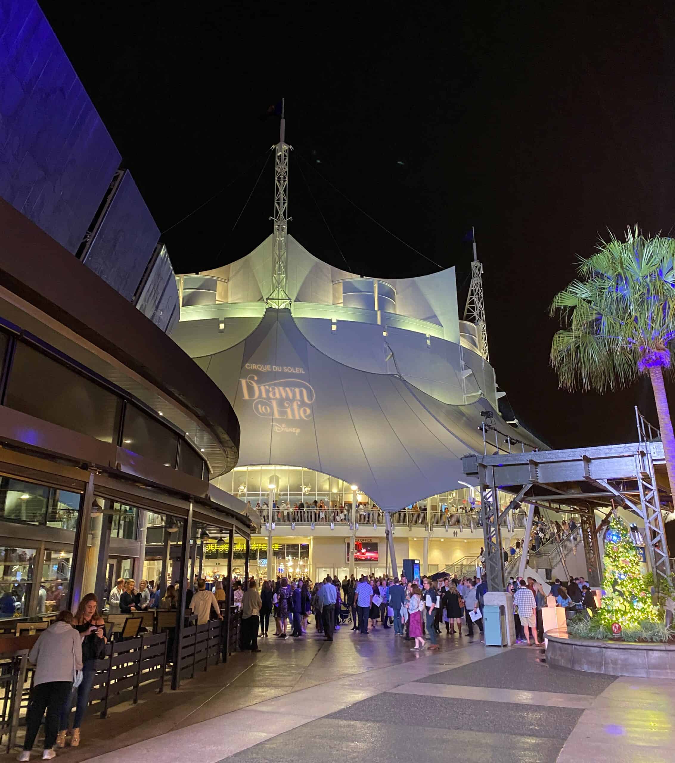 Cirque du Soleil Disney Springs Theater is a large white tent-like building at the edge of Disney Springs with restaurants nearby
