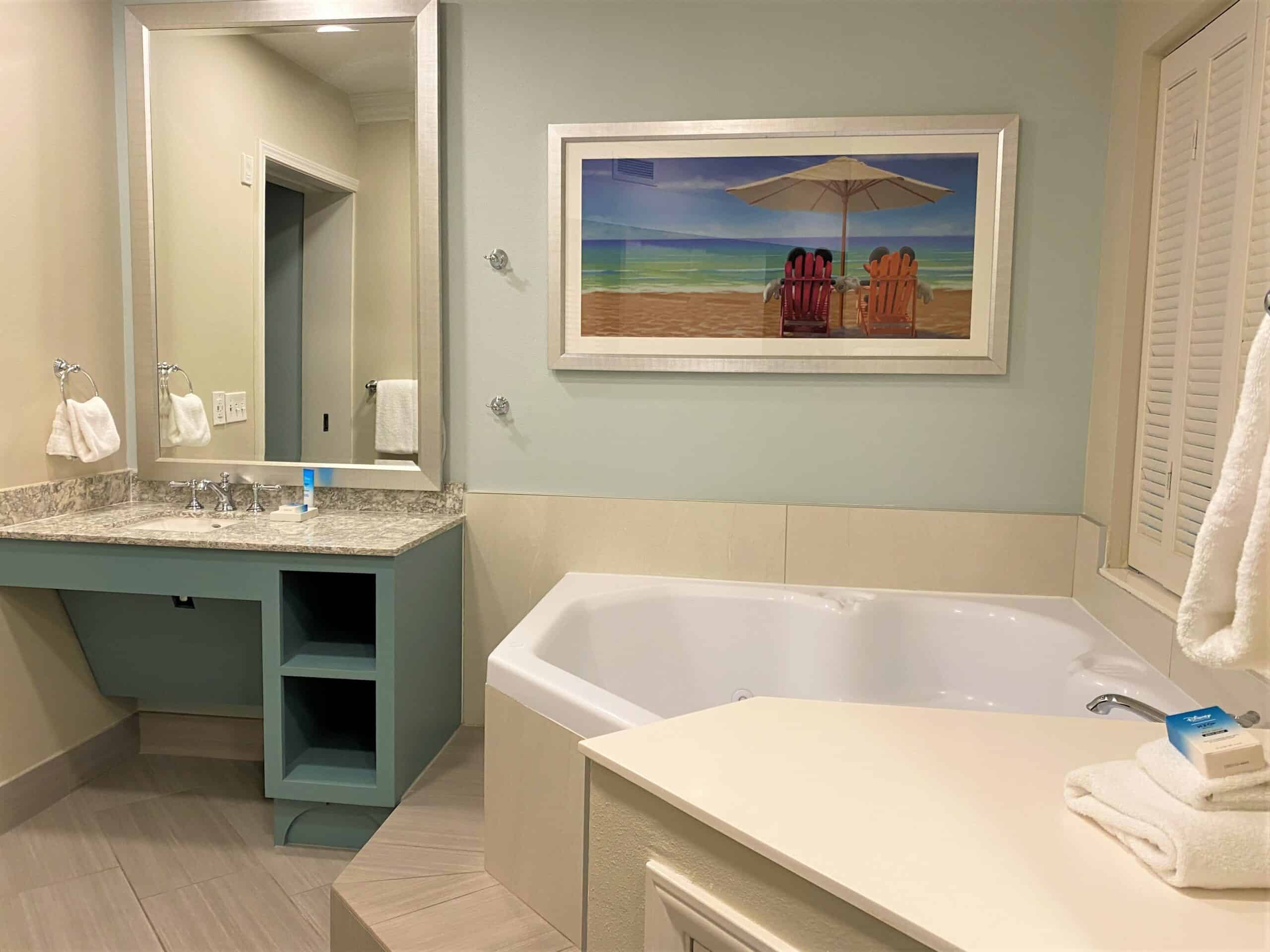 Disney's Old Key West Master Bathroom features a large soaking tub and spacious sink area with tropical touches, Mickey and Minnie on the beach wall art, and soft blue hues