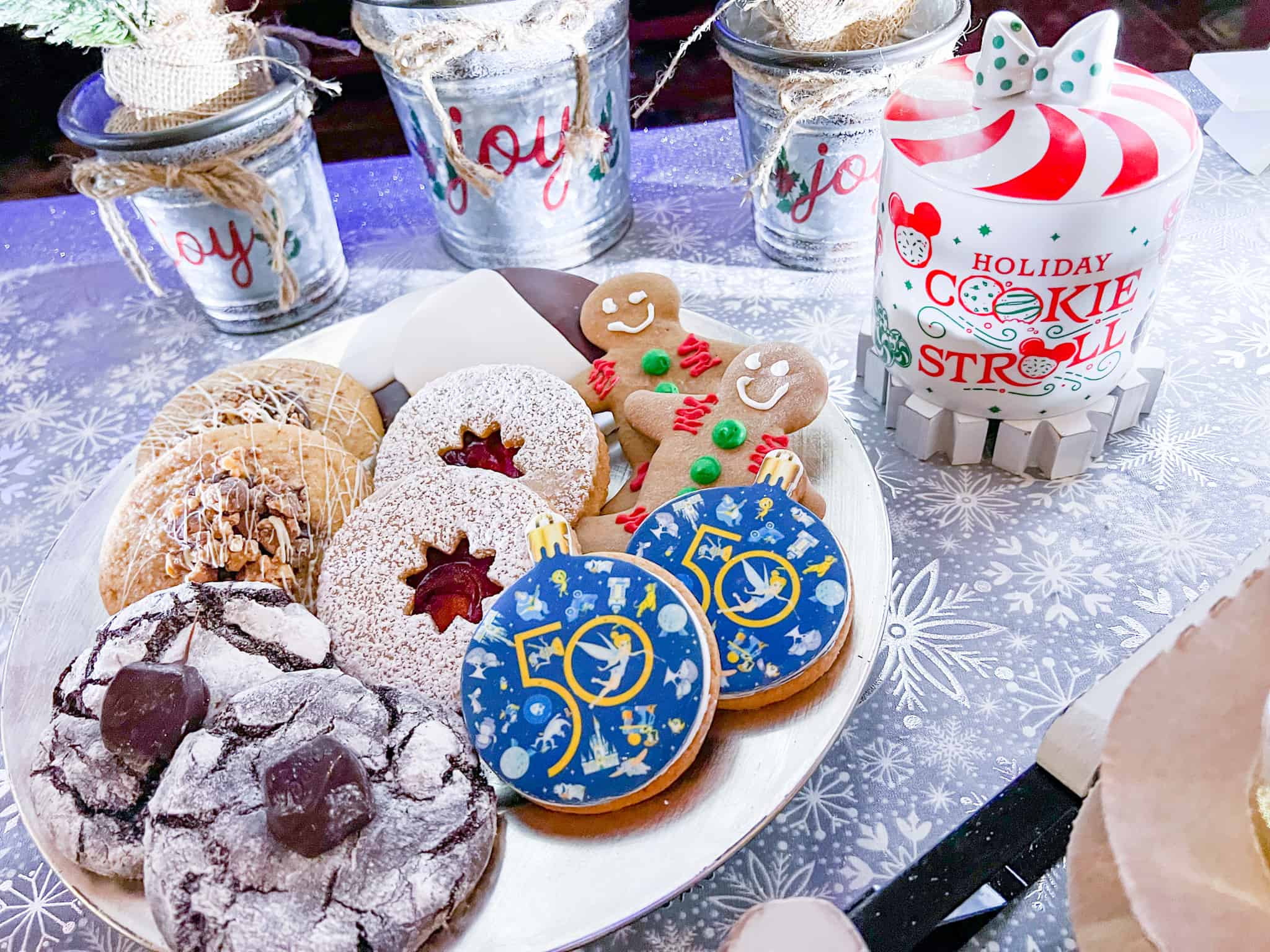 A variety of cookies from the EPCOT Holiday Cookie Stroll are on a white platter and a peppermint style cookie jar is next to the platter