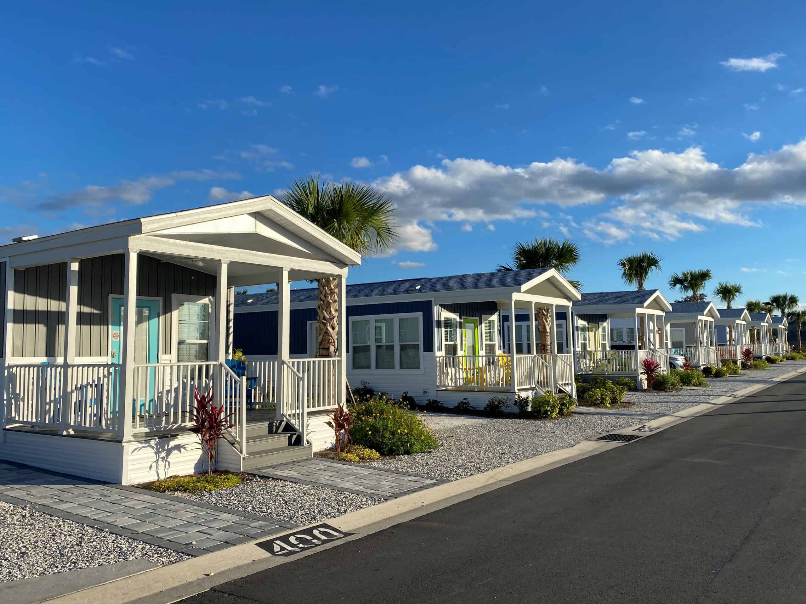 One Bedroom Cottages at Cabana Club Resort Florida line the streets of the resort. They have metal siding in soft gray colors, a white wood front porch, and brightly colored doors and deck chairs.