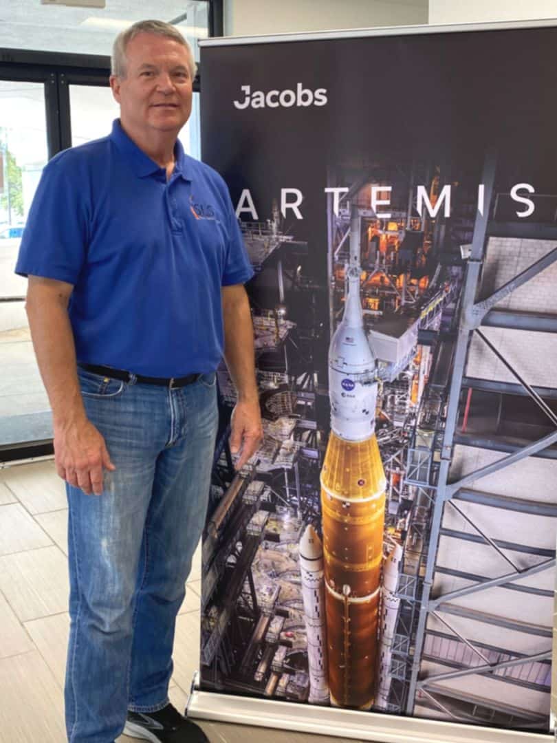 Randy Lycans - Vice President, Jacobs Engineering Group stands in front of a banner with a photo of the Space Launch System on the launch pad for the Artemis Program