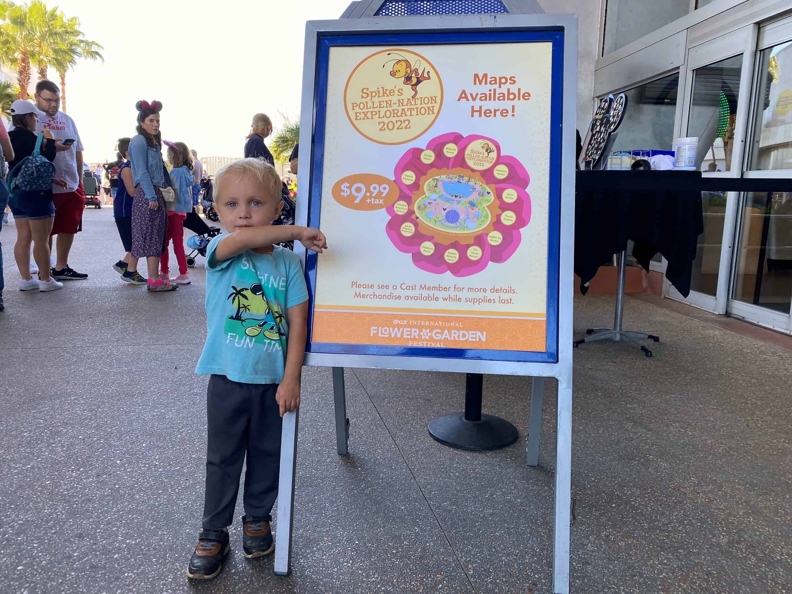 a four year old boy stands in front of a sign for Spike's Pollen-Nation Exploration Scavenger Hunt Flower and Garden 2022