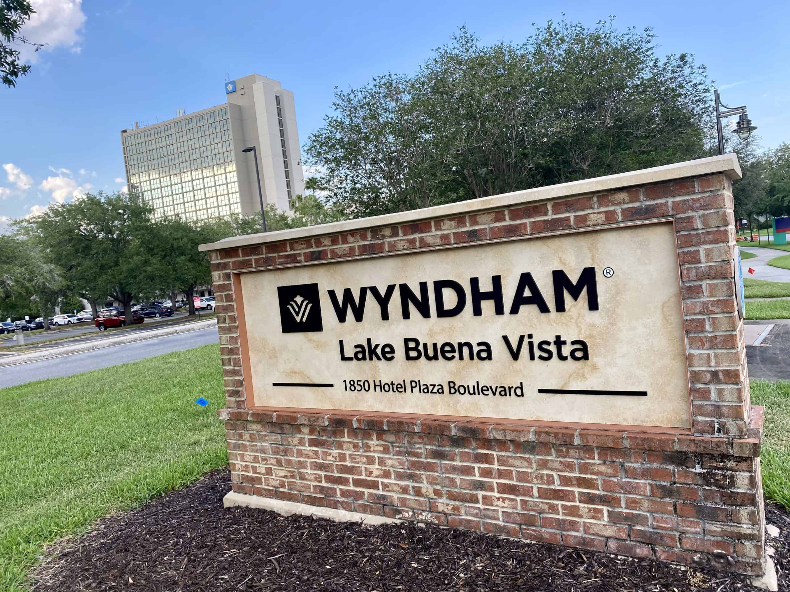 Wyndham Lake Buena Vista Exterior's is beige and tall, reflecting the nearby Disney Springs area. A sign made of bricks showcasing the name of the hotel, Wyndham Lake Buena Vista, stands along the walkway that leads to Disney Springs