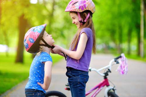 Safety Awareness Tips for Parents: a girl fastens another girl's bike helmet.