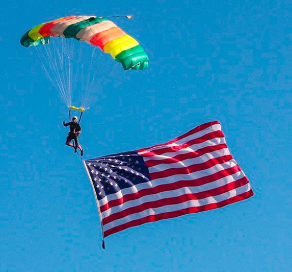 Parachutist from The Chuters descends with a colorful parachute and a large American flag during the Gasparilla Air Invasion in Tampa.