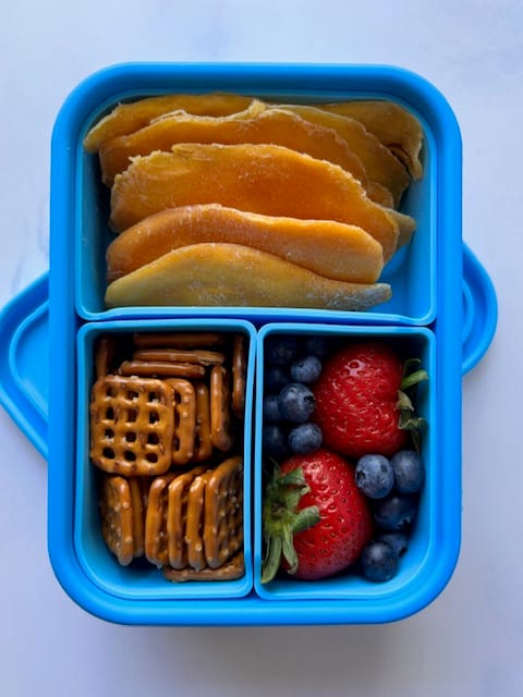 Lunchboxmafia healthy snack with mango slicex, pretzels and berries.