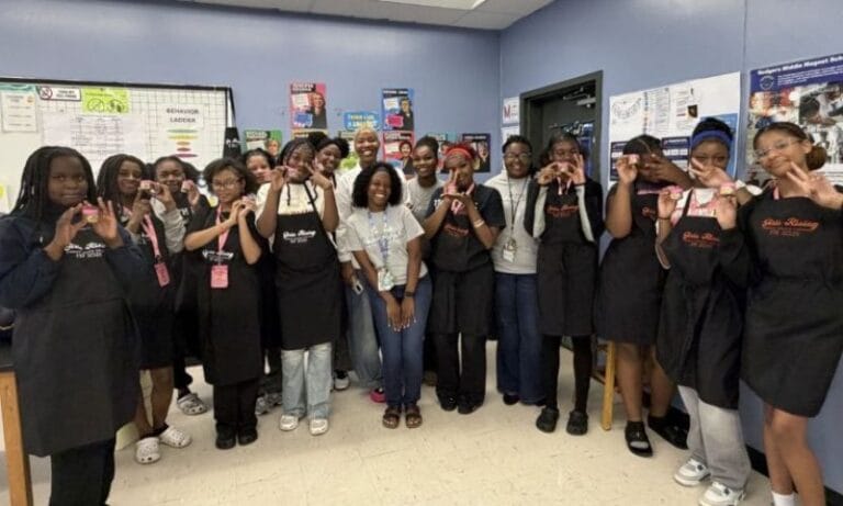 Young girls standing together wearing aprons in a classroom after creating their own body scrub