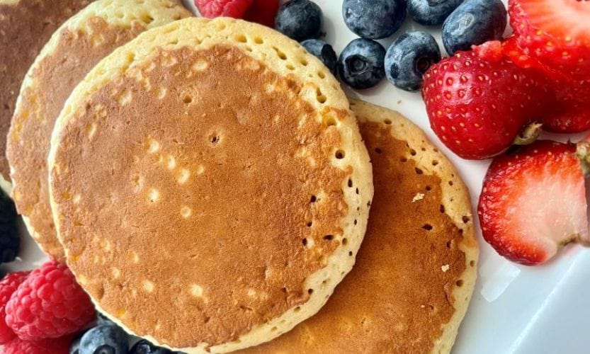pancakes on a plate with blueberries and strawberries on the side