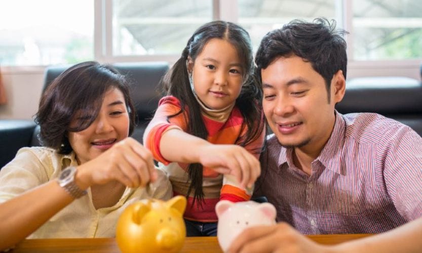 A family sitting down putting money into piggy banks on the table