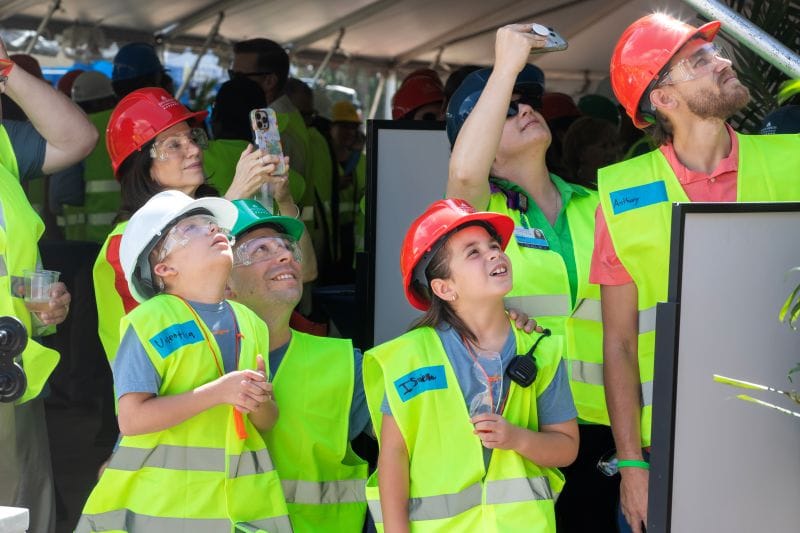 Spectators in neon construction vests watch the last beams being hoisted to the top of the new Johns Hopkins All children's Wesley Chapel