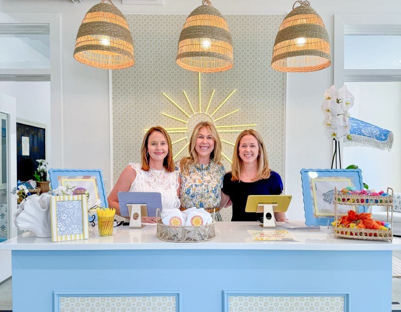 Sunshine Needlepoint Owners Heather Barrow, Elizabeth Lee, and Courtney Lang posing behind the counter